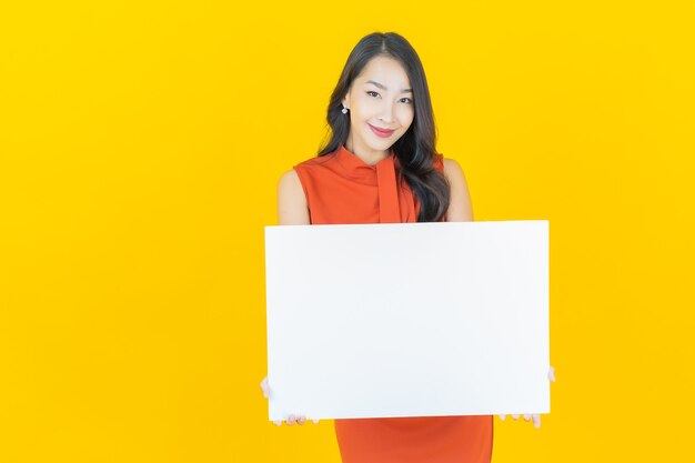 Retrato hermosa joven asiática con cartelera blanca vacía en amarillo