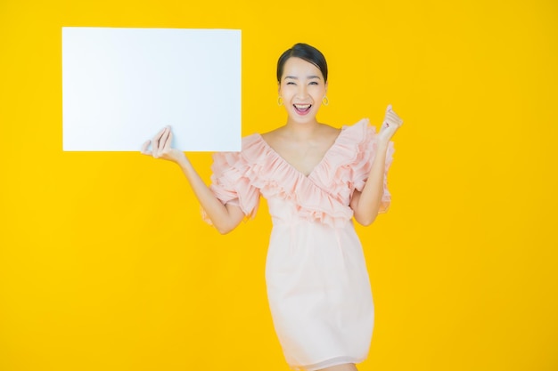 Retrato hermosa joven asiática con cartelera blanca vacía en amarillo