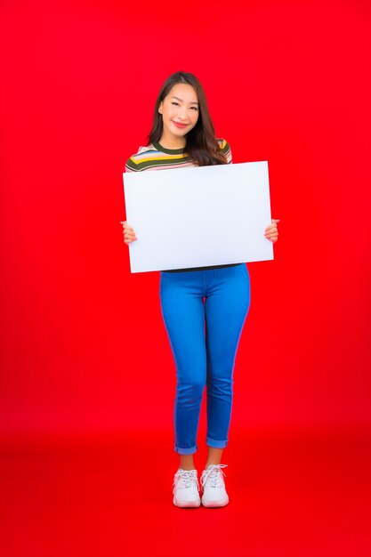 Retrato hermosa joven asiática con cartelera vacía blanca en la pared roja