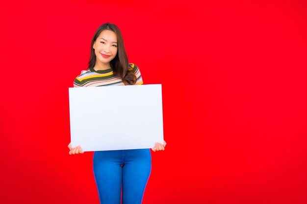 Retrato hermosa joven asiática con cartelera vacía blanca en la pared roja