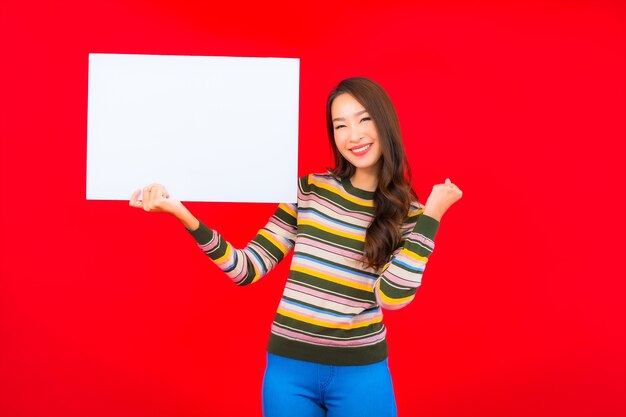 Retrato hermosa joven asiática con cartelera vacía blanca en la pared roja