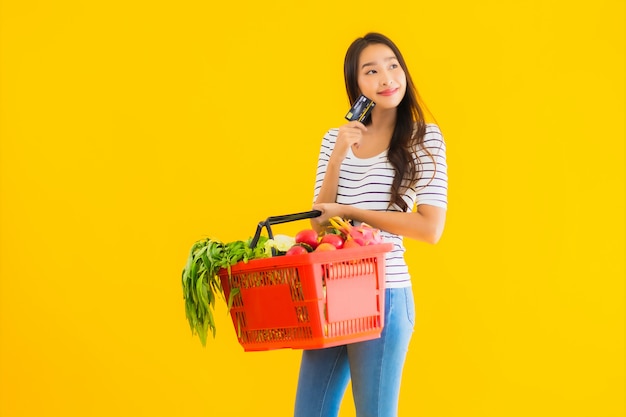 Retrato hermosa joven asiática con cesta de la compra y carrito de supermercado