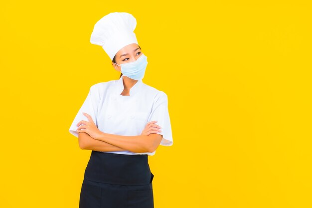 Retrato hermosa joven asiática chef usar máscara para proteger covid19 o coronavirus sobre fondo amarillo aislado