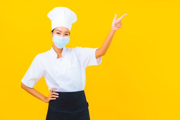Retrato hermosa joven asiática chef usar máscara para proteger covid19 o coronavirus sobre fondo amarillo aislado