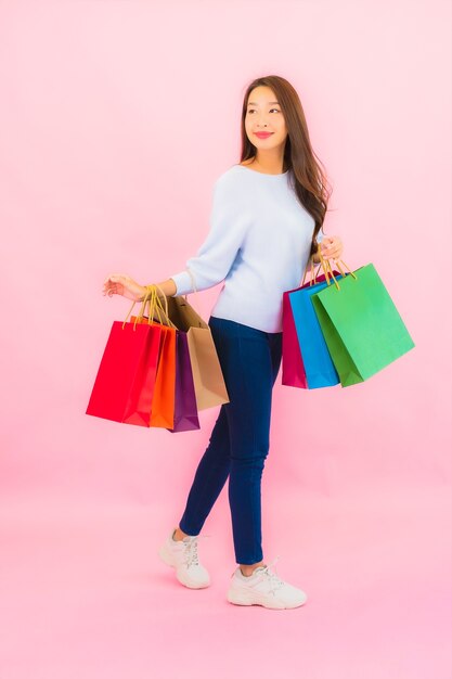 Retrato hermosa joven asiática con colorido bolso de compras en pared aislada de color rosa