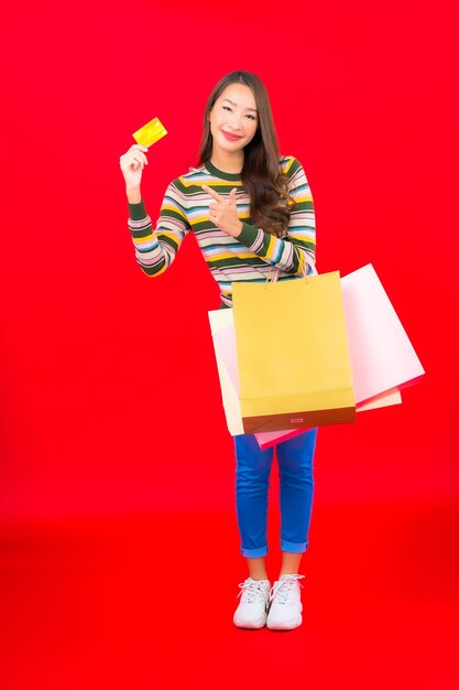 Retrato hermosa joven asiática con colorido bolso de compras y tarjeta de crédito en la pared roja