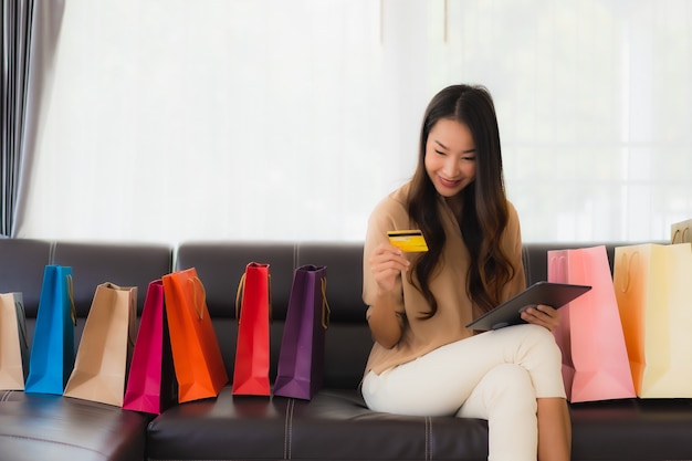 Retrato de hermosa joven asiática compras en línea con tarjeta de crédito y teléfono inteligente alrededor de bolsas de compras