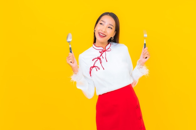 Foto gratuita retrato hermosa joven asiática con cuchara y tenedor en amarillo