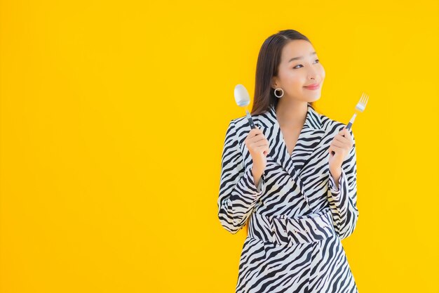 Retrato hermosa joven asiática con cuchara y tenedor listo para comer en amarillo