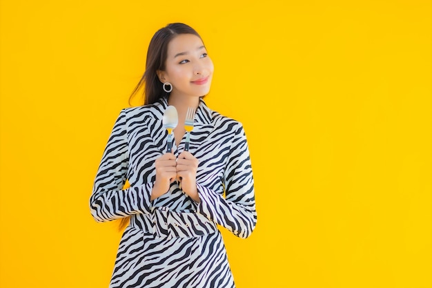 Retrato hermosa joven asiática con cuchara y tenedor listo para comer en amarillo