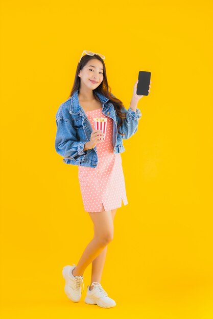 Retrato hermosa joven asiática disfruta feliz con palomitas de maíz teléfono y ver película
