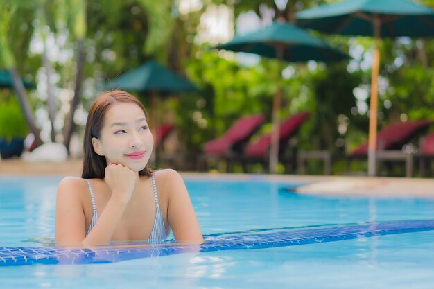 Retrato hermosa joven asiática disfruta relajarse sonrisa ocio alrededor de la piscina al aire libre en el hotel