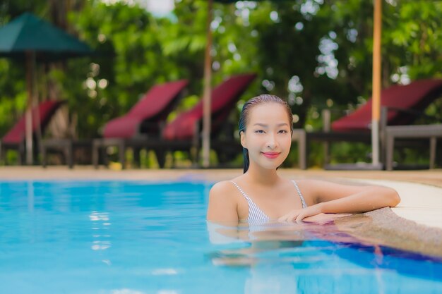 Retrato hermosa joven asiática disfruta relajarse sonrisa ocio alrededor de la piscina al aire libre en el hotel