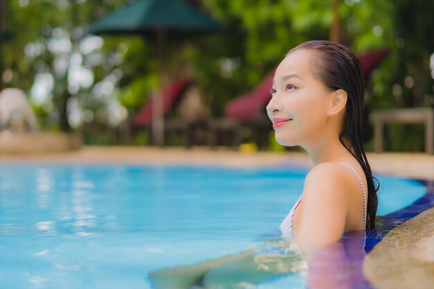 Retrato hermosa joven asiática disfruta relajarse sonrisa ocio alrededor de la piscina al aire libre en el hotel