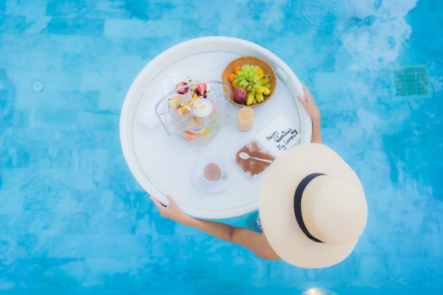 Retrato hermosa joven asiática disfrutar con té de la tarde o desayuno flotando en la piscina