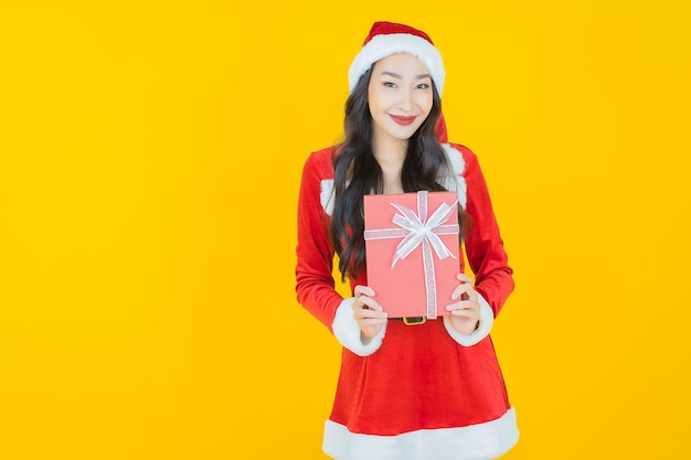 Retrato hermosa joven asiática llevar traje de navidad con caja de regalo roja sobre amarillo