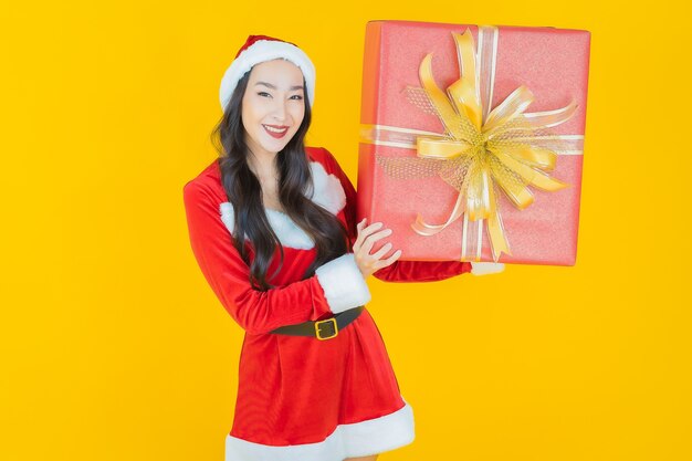 Retrato hermosa joven asiática llevar traje de navidad con caja de regalo roja sobre amarillo