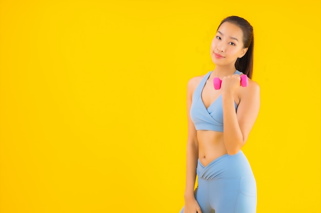 Retrato hermosa joven asiática con mancuernas y ropa deportiva en amarillo