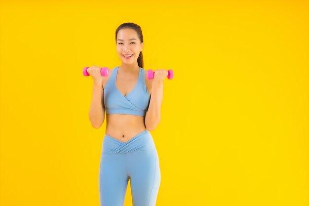 Retrato hermosa joven asiática con mancuernas y ropa deportiva en amarillo