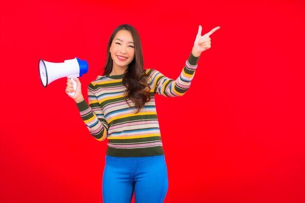 Retrato hermosa joven asiática con megáfono para comunicación en pared roja