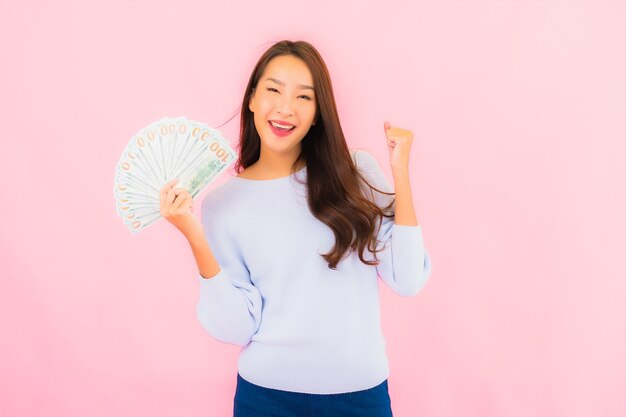 Retrato hermosa joven asiática con mucho dinero en efectivo y dinero en la pared de color rosa