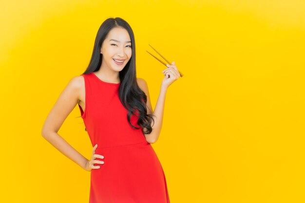 Retrato hermosa joven asiática con palillos listos para comer en la pared amarilla