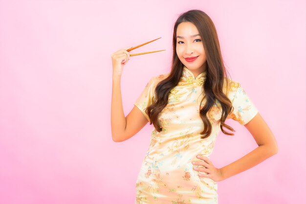 Retrato hermosa joven asiática con palillos en la pared rosa
