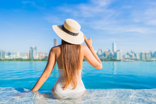 Retrato hermosa joven asiática relajante alrededor de la piscina al aire libre con vistas a la ciudad