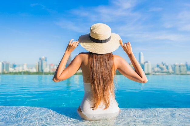 Retrato hermosa joven asiática relajante alrededor de la piscina al aire libre con vistas a la ciudad