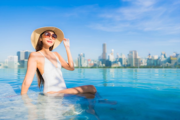 Retrato hermosa joven asiática relajante alrededor de la piscina al aire libre con vistas a la ciudad