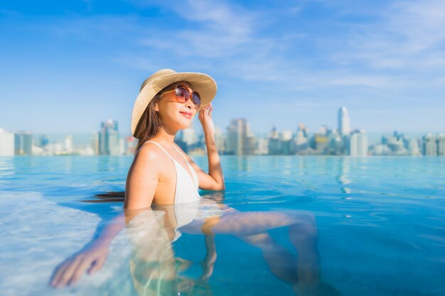 Retrato hermosa joven asiática relajante alrededor de la piscina al aire libre con vistas a la ciudad