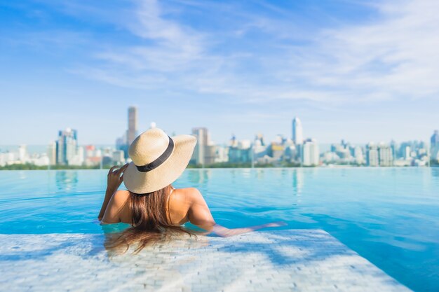 Retrato hermosa joven asiática relajante alrededor de la piscina al aire libre con vistas a la ciudad