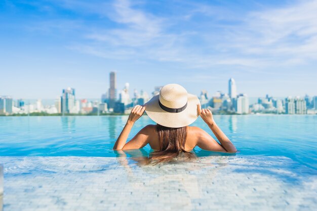 Retrato hermosa joven asiática relajante alrededor de la piscina al aire libre con vistas a la ciudad