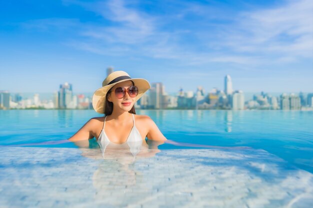 Retrato hermosa joven asiática relajante alrededor de la piscina al aire libre con vistas a la ciudad