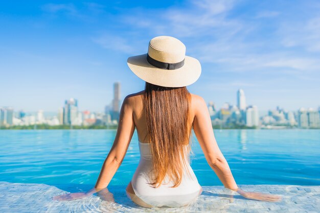 Retrato hermosa joven asiática relajante alrededor de la piscina al aire libre con vistas a la ciudad