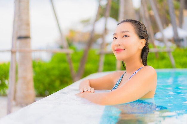 Retrato hermosa joven asiática relajarse ocio alrededor de la piscina al aire libre con mar océano playa