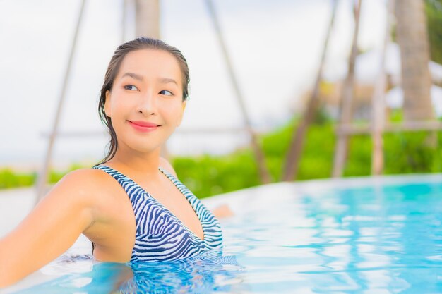 Retrato hermosa joven asiática relajarse ocio alrededor de la piscina al aire libre con mar océano playa