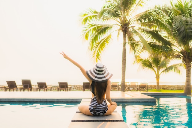 Retrato hermosa joven asiática relajarse en la piscina al aire libre en el hotel resort con palmera al atardecer o al amanecer