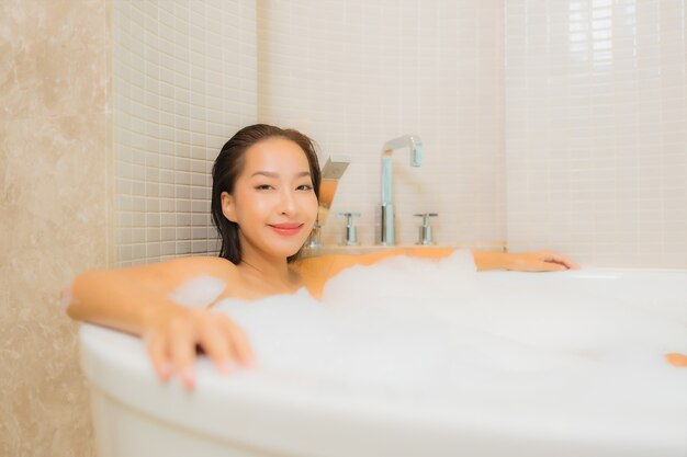 Retrato hermosa joven asiática relajarse sonrisa en la bañera en el interior del baño