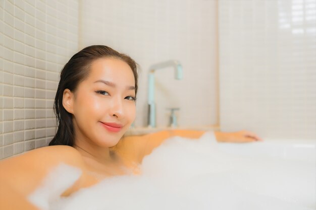 Retrato hermosa joven asiática relajarse sonrisa en la bañera en el interior del baño