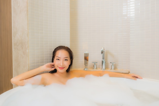 Retrato hermosa joven asiática relajarse sonrisa en la bañera en el interior del baño