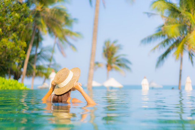 Retrato hermosa joven asiática relajarse sonrisa disfrutar de ocio alrededor de la piscina cerca de la playa con vistas al mar en vacaciones