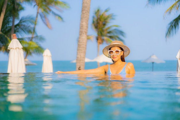 Retrato hermosa joven asiática relajarse sonrisa disfrutar de ocio alrededor de la piscina cerca de la playa con vistas al mar en vacaciones