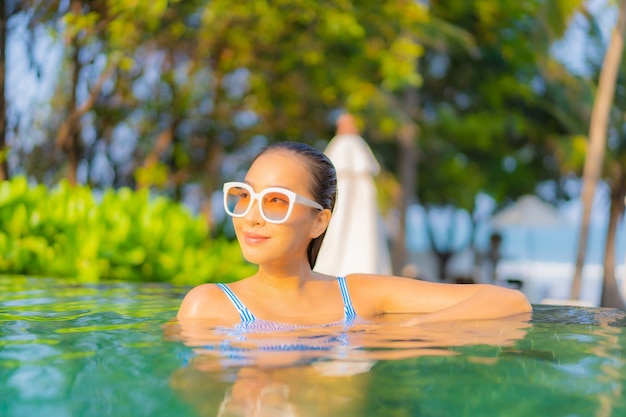 Retrato hermosa joven asiática relajarse sonrisa disfrutar de ocio alrededor de la piscina cerca de la playa con vistas al mar en vacaciones