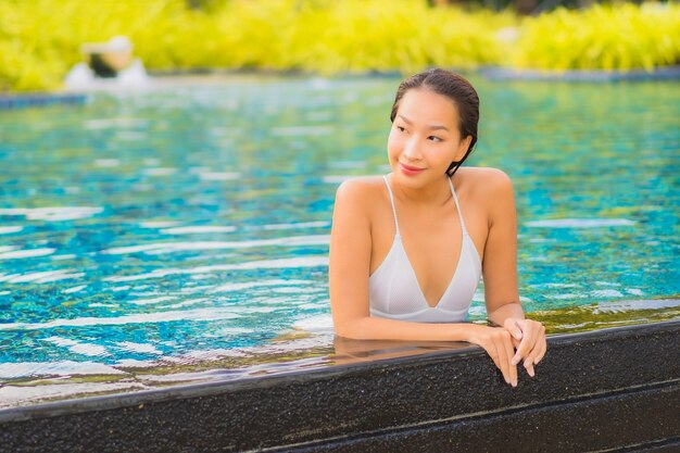 Retrato hermosa joven asiática relajarse sonrisa ocio alrededor de la piscina al aire libre cerca del mar