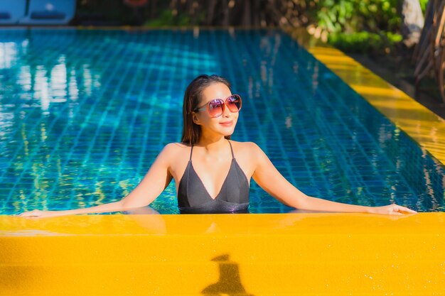 Retrato hermosa joven asiática relajarse sonrisa ocio alrededor de la piscina al aire libre cerca del mar