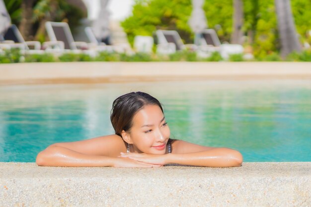 Retrato hermosa joven asiática relajarse sonrisa ocio alrededor de la piscina al aire libre con mar océano en vacaciones de viaje