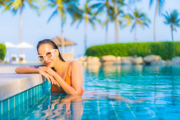 Retrato hermosa joven asiática relajarse sonrisa ocio alrededor de la piscina al aire libre con vista al mar