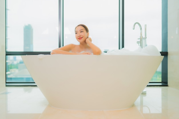 Retrato hermosa joven asiática relajarse sonrisa ocio en la bañera en el interior del baño