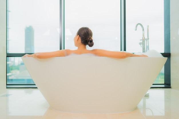 Retrato hermosa joven asiática relajarse sonrisa ocio en la bañera en el interior del baño